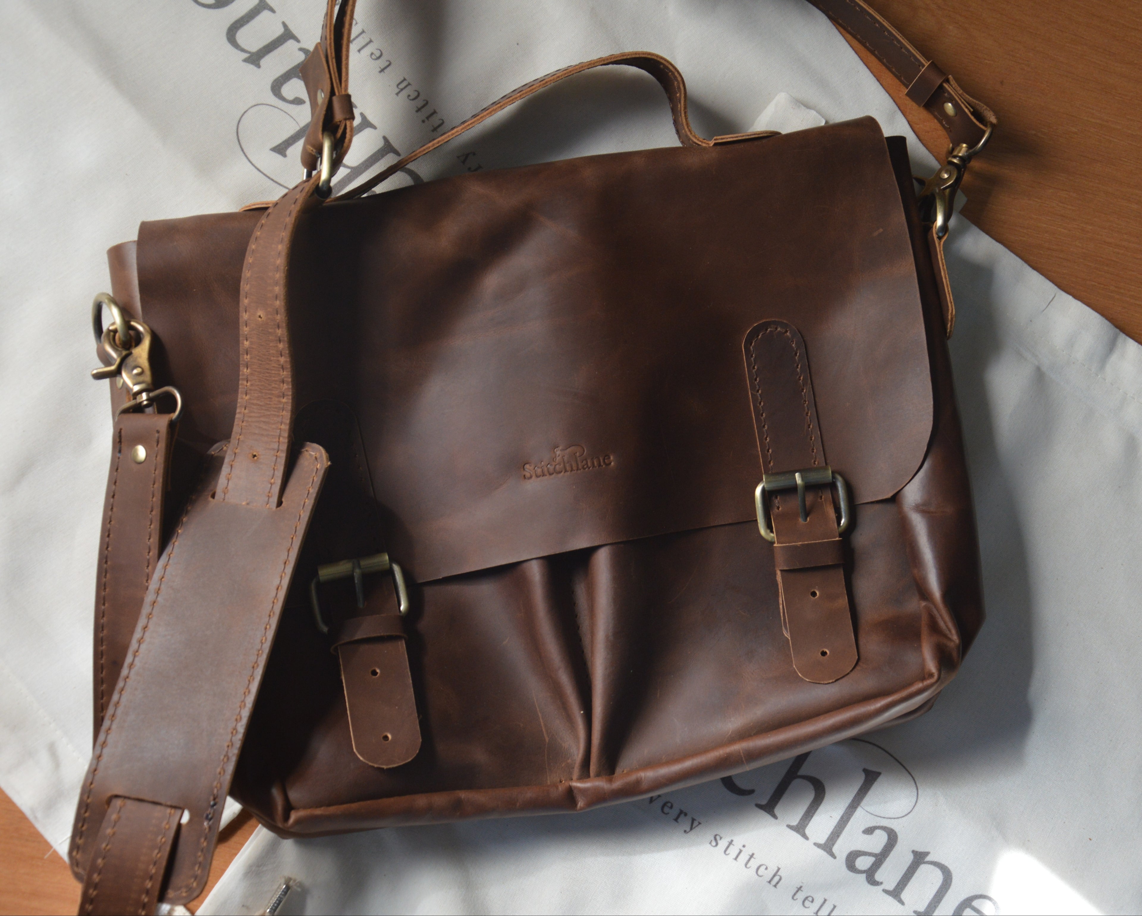 Brown leather satchel bag on a white surface with visible branding.