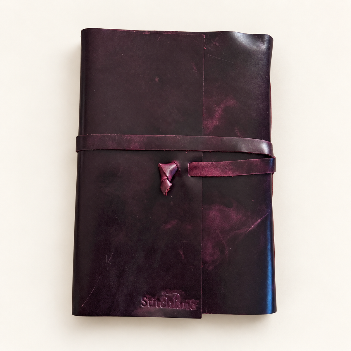 A dark purple leather journal -notebook with a matching wrap-around strap and small leather tie, photographed flat on a light cream background. The brand name 'Streichlang' is embossed on the bottom corner.