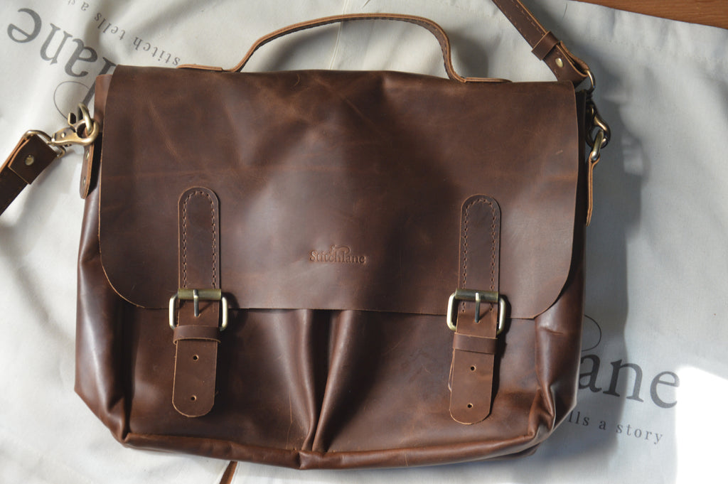 Brown leather satchel bag with gold buckles on a light gray background