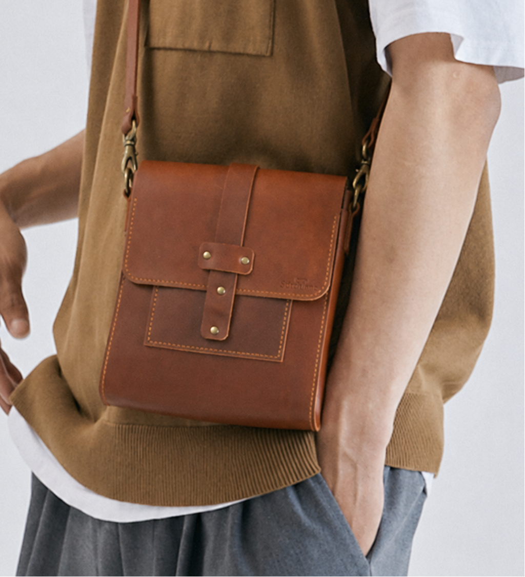 Person wearing a brown vest with a matching leather bag on a white background