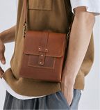 Person wearing a brown vest with a matching leather bag on a white background